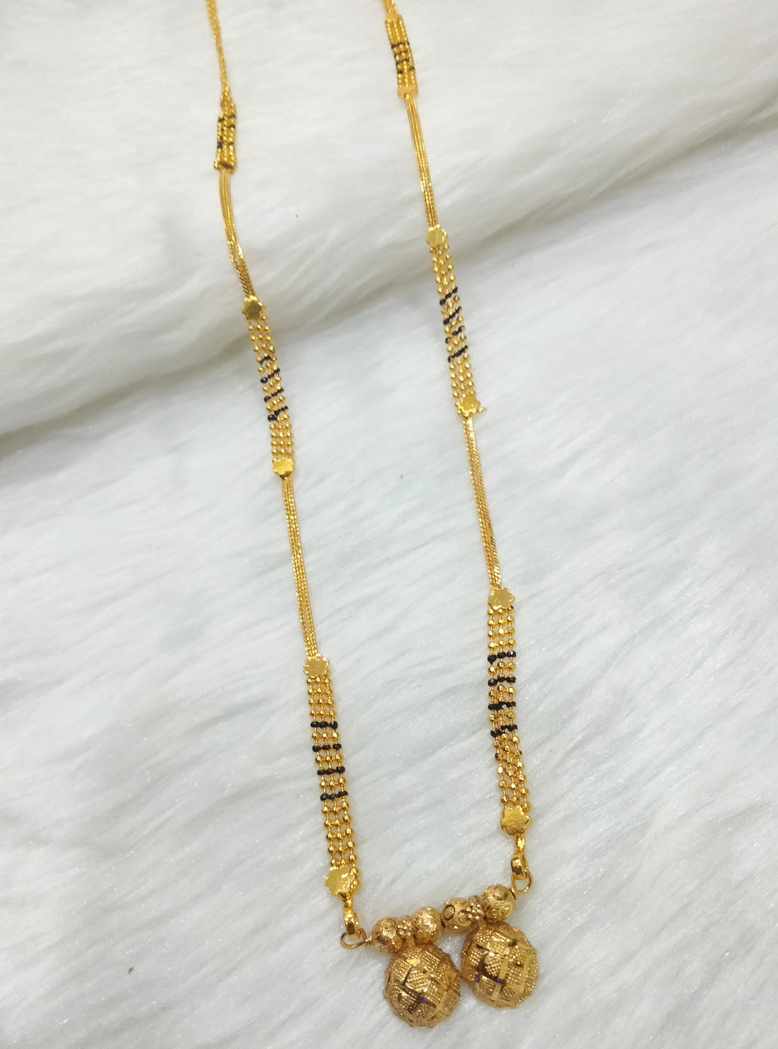 A long 30-inch Maharashtrian Vati Mangalsutra made of gold with black beads and a double-sphere pendant.