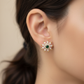 Close-up of an ear wearing a decorative earring with pearls and a green gemstone.