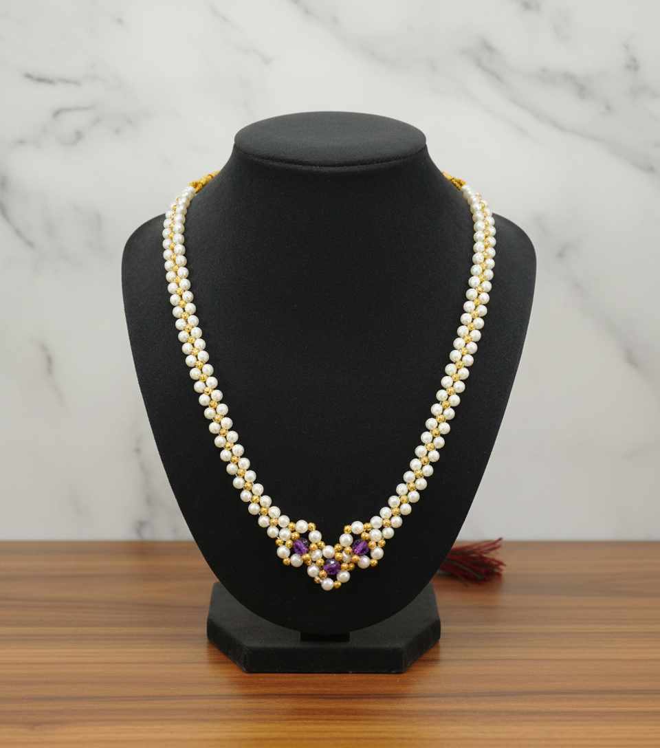 Pearl necklace with gold and purple accents on a black mannequin bust against a marble background.