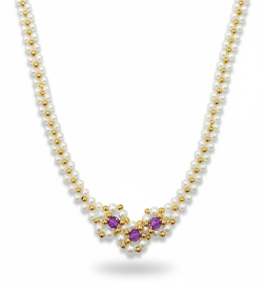 Pearl necklace with gold and purple accents on a black mannequin bust against a marble background.
